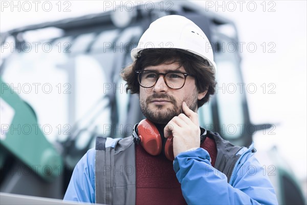 Young engineer with helmet and hearing protection checks outside work with laptop