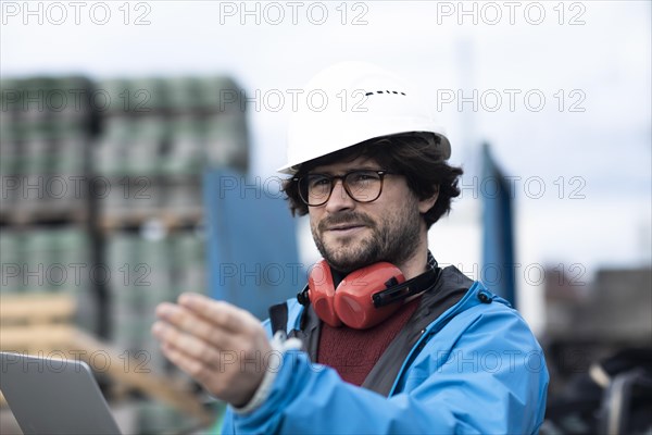 Young engineer wearing a helmet and hearing protection at a workstation outside on a construction site with a laptop
