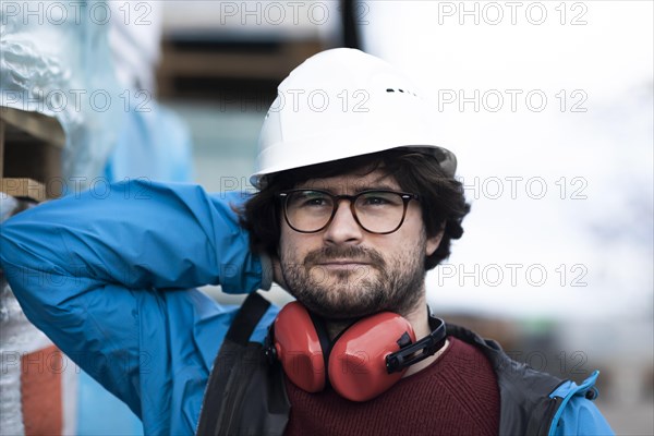 Young engineer with helmet and hearing protection at a work site outside