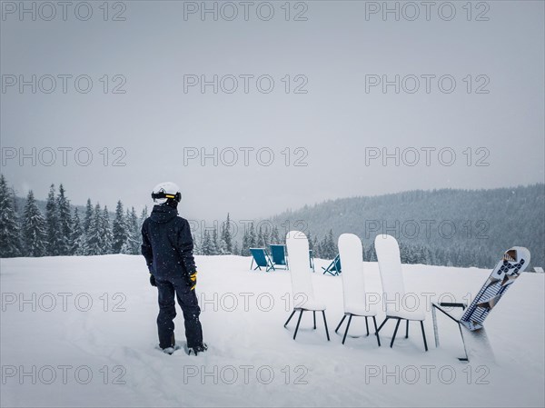 Rear view of a skier on the top of a mountain looking at the snow covered fir forest on the horizon. Snowy winter day