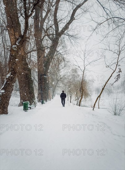 Solitary man silhouette wandering a snowy walkway in the winter park. Calm and moody scene