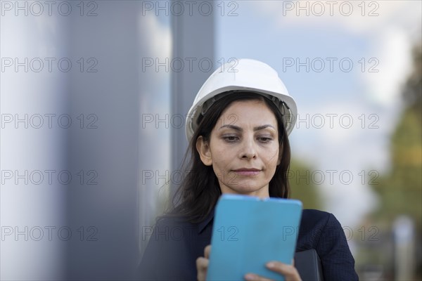 Middle-aged woman with dark hair and helmet checks a plant with a tablet