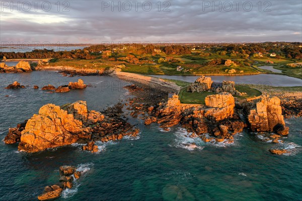 Drone shot from the Atlantic Ocean onto the granite coast of Plougrescant with a view of the house between the rocks (Le gouffre de Plougrescant) at sunset