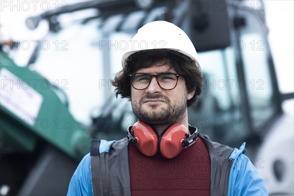 Young engineer with helmet and hearing protection checks outside work with laptop