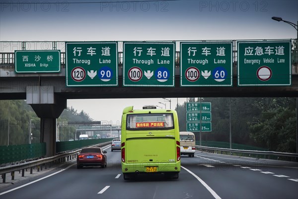 Bus travelling on 3-lane motorway with signs and a bridge