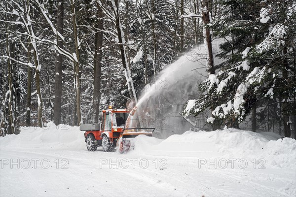 Holder C9700H municipal tractor with snow blower clearing snow from the road in the forest after heavy snowfall in winter