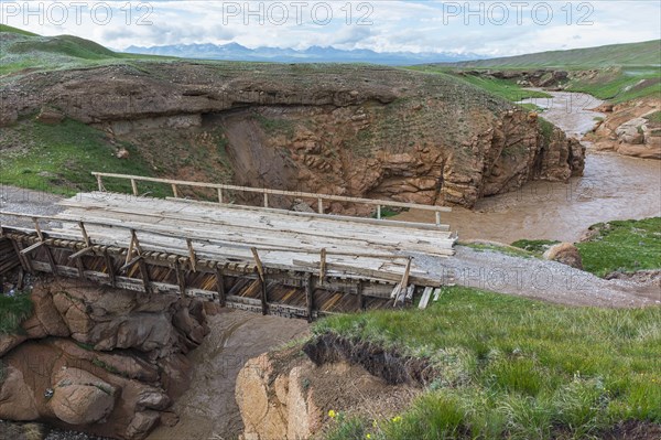 Wooden bridge over a muddy river flowing in a wild gorge