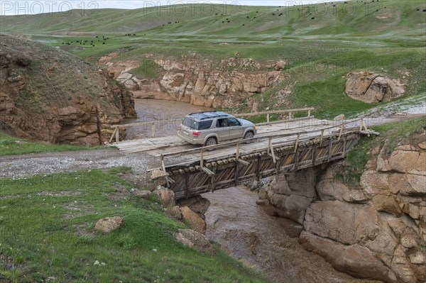 Off-road vehicle crossing a wooden bridge over a wild gorge