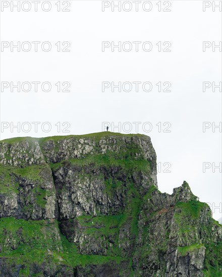 A person stands on a cliff in the distance