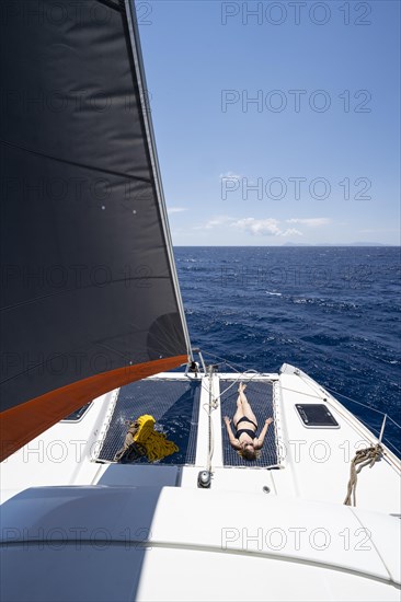 Young woman lying in the net on the deck of a sailing catamaran