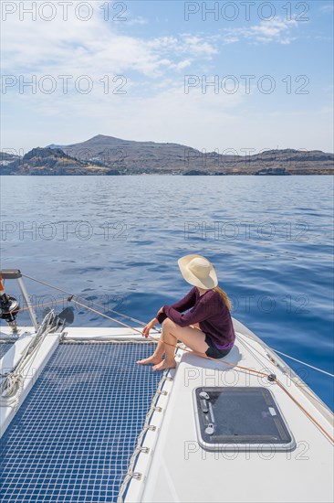 Young woman with hat sitting on deck at the net of a sailing catamaran