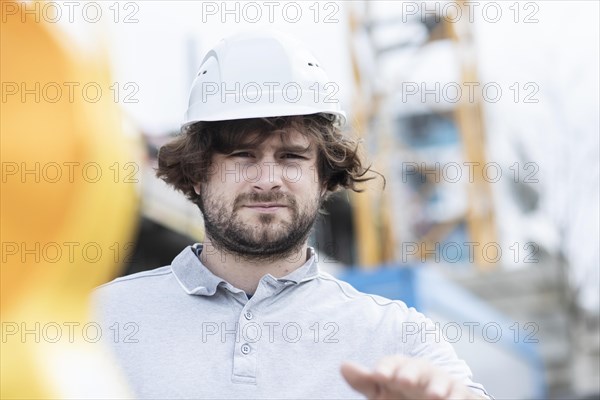 Technician with beard middle aged and wearing polo shirt and helmet outside at work