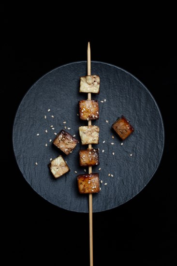 Fried tofu cubes with wooden skewer on plate