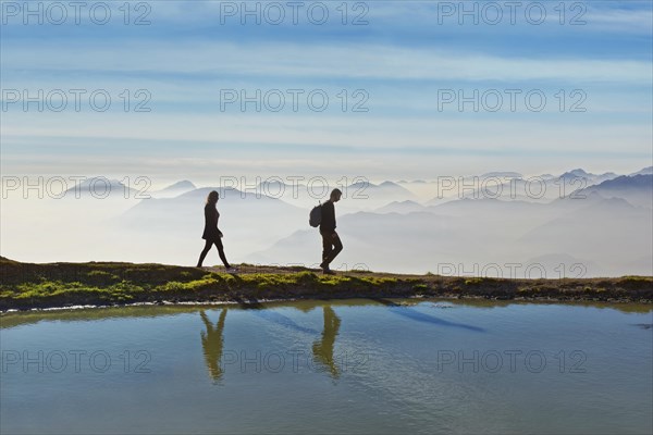 Hikers on a small lake with the peaks of the Lake Garda mountains and Bergamo Alps