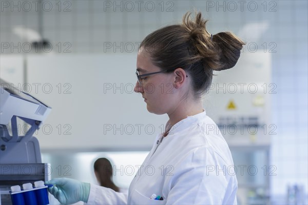 Young lab technician wearing a face mask and pipetting a sample in a laboratory with laboratory equipment at a workflow