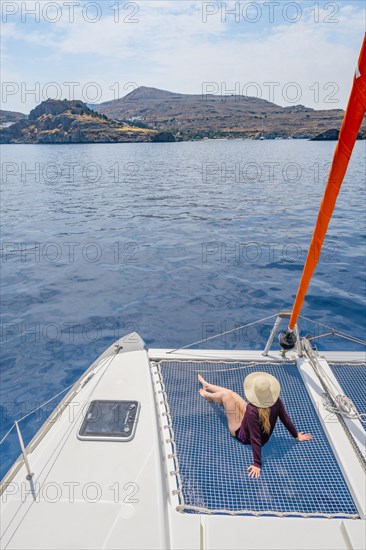 Young woman with hat sitting in the net of a sailing catamaran