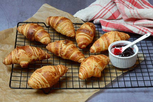 Several croissants on baking rack and bowl with jam