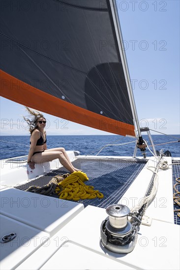 Young woman in bikini sitting in the net of a sailing catamaran