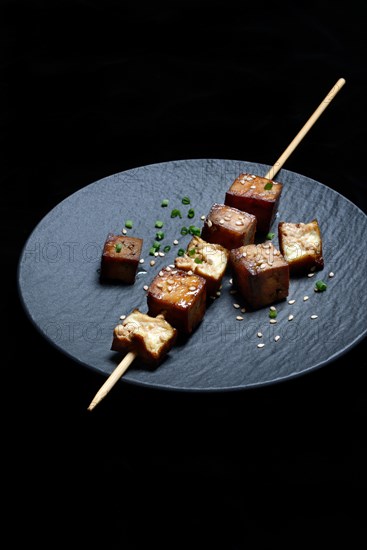 Fried tofu cubes with wooden skewer on plate