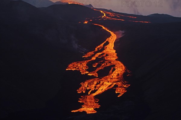 Glowing lava flows partly down mountainside