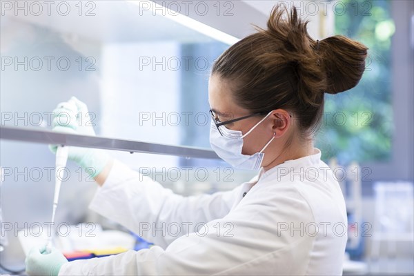 Young lab technician wearing a face mask and pipetting a sample in a laboratory with laboratory equipment at a workflow