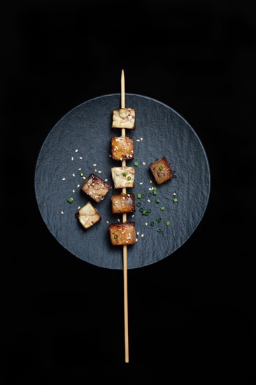 Fried tofu cubes with wooden skewer on plate