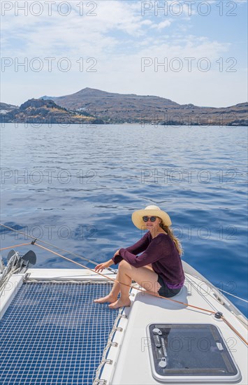 Young woman sitting on deck at the net of a sailing catamaran