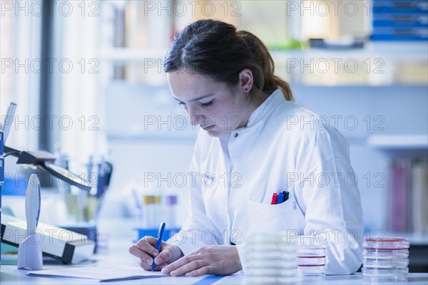 Lab technician with sample in petri dish works in a lab with lab equipment and writes protocol