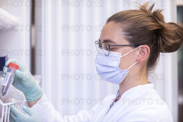 Young lab technician with mouth guard and sample in tube working in a lab with refrigerator