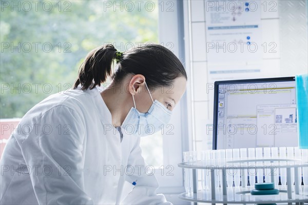 Young chemist with sample and laboratory glasses working in a laboratory with laboratory equipment and monitor