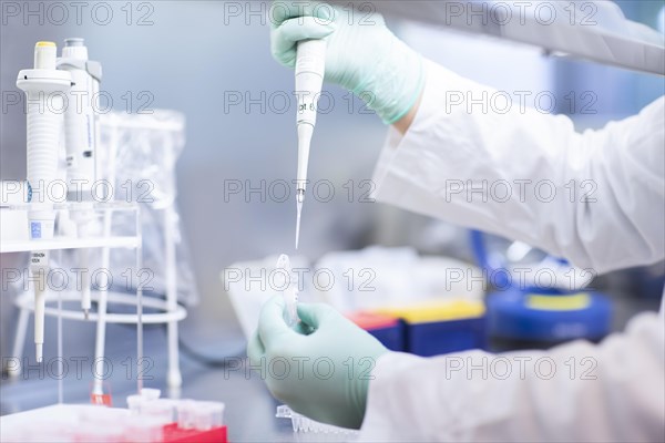 Young lab technician wearing a face mask and pipetting a sample in a laboratory with laboratory equipment at a workflow