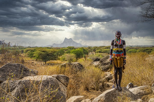 Traditional dressed young girl from the Laarim tribe standing on a rock