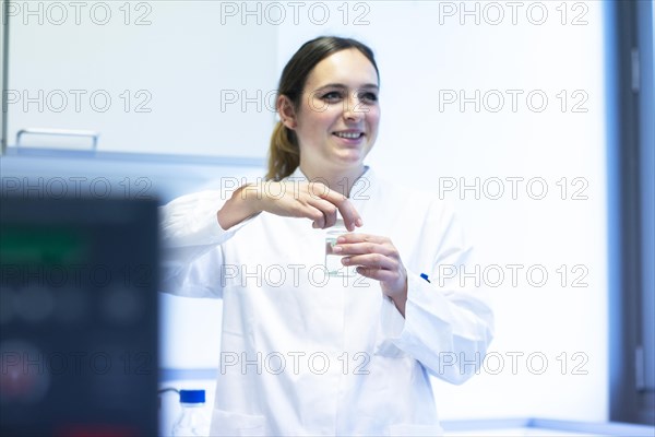 Young laboratory assistant with sample and laboratory glasses working in a laboratory with laboratory equipment