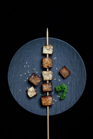 Fried tofu cubes with wooden skewer on plate