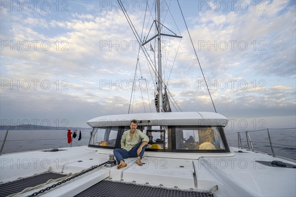 Young man sitting on the deck of a sailing catamaran