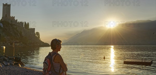Hiker on the shore in front of Castello Scaligero at sunset