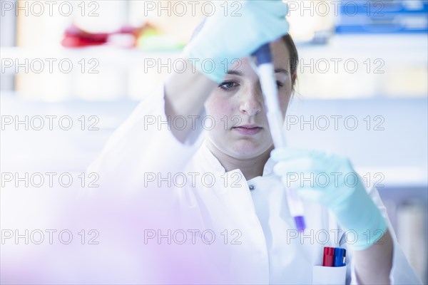 Lab technician with pipette and sample in petri dish working in a lab with lab equipment