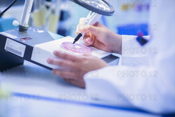 Lab technician with sample in petri dish working in a lab with lab equipment