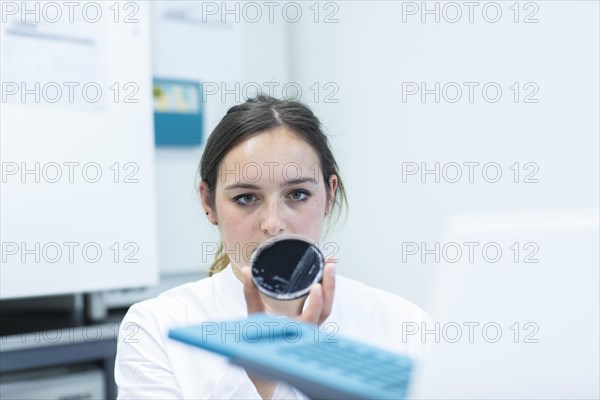 Young laboratory assistant with sample on petridish works in a laboratory with laboratory equipment