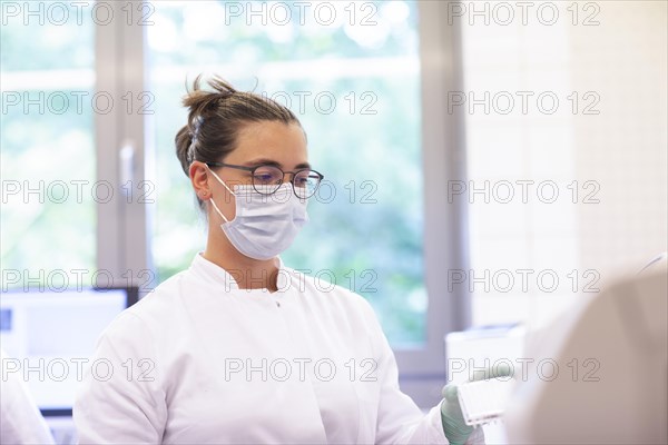 Young lab technician with mouth guard and sample in tubes working in a lab with lab equipment