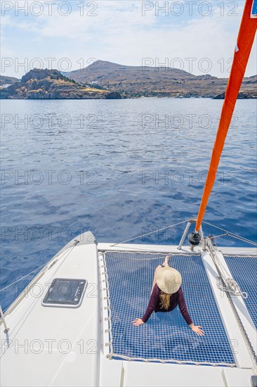 Young woman with hat sitting in the net of a sailing catamaran