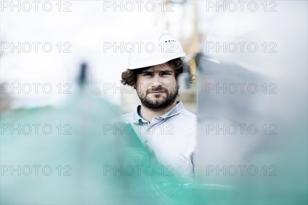 Technician with beard middle aged and wearing polo shirt and helmet outside at work