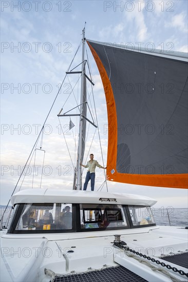 Young man standing between the sails of a sailing catamaran