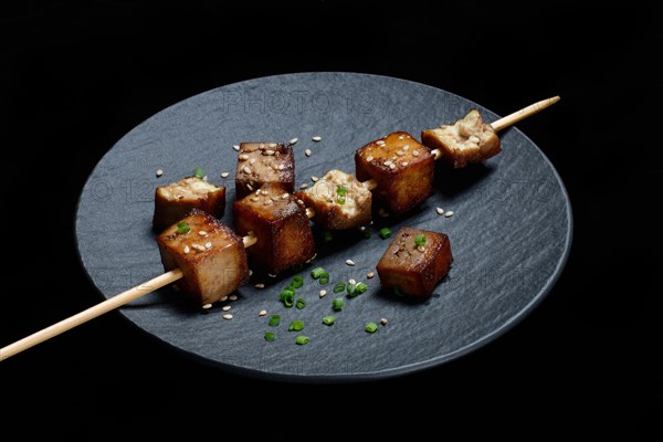 Fried tofu cubes with wooden skewer on plate