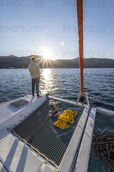 Young man standing on a catamaran looking into the sunset