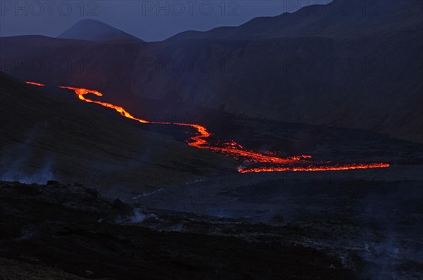 Glowing lava flows partly down mountainside