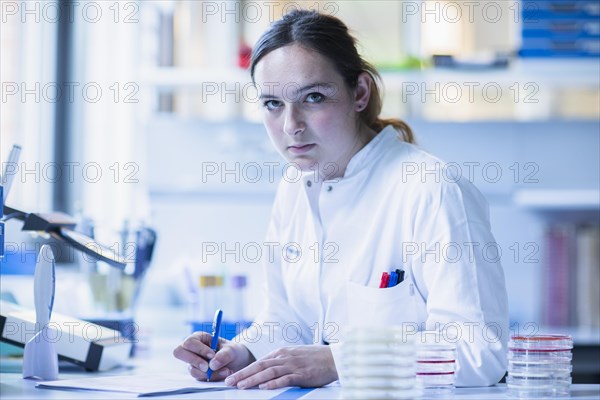 Lab technician with sample in petri dish works in a lab with lab equipment and writes protocol
