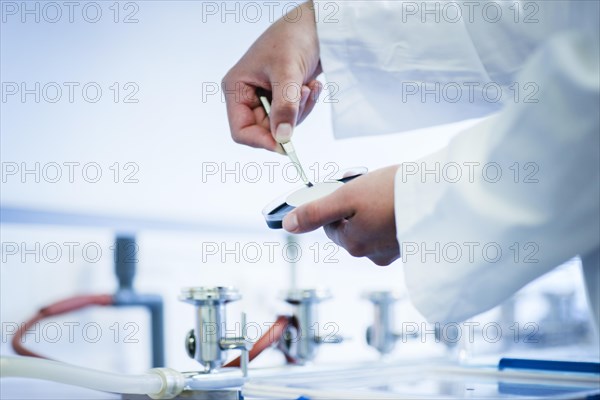 Young laboratory assistant with sample and tweezers working in a laboratory with laboratory equipment