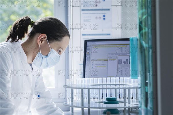 Young chemist with sample and laboratory glasses working in a laboratory with laboratory equipment and monitor