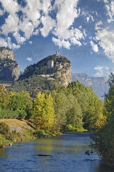 Small idyllic river Sarca with the medieval castle ruin Castello di Arco towering on a castle rock
